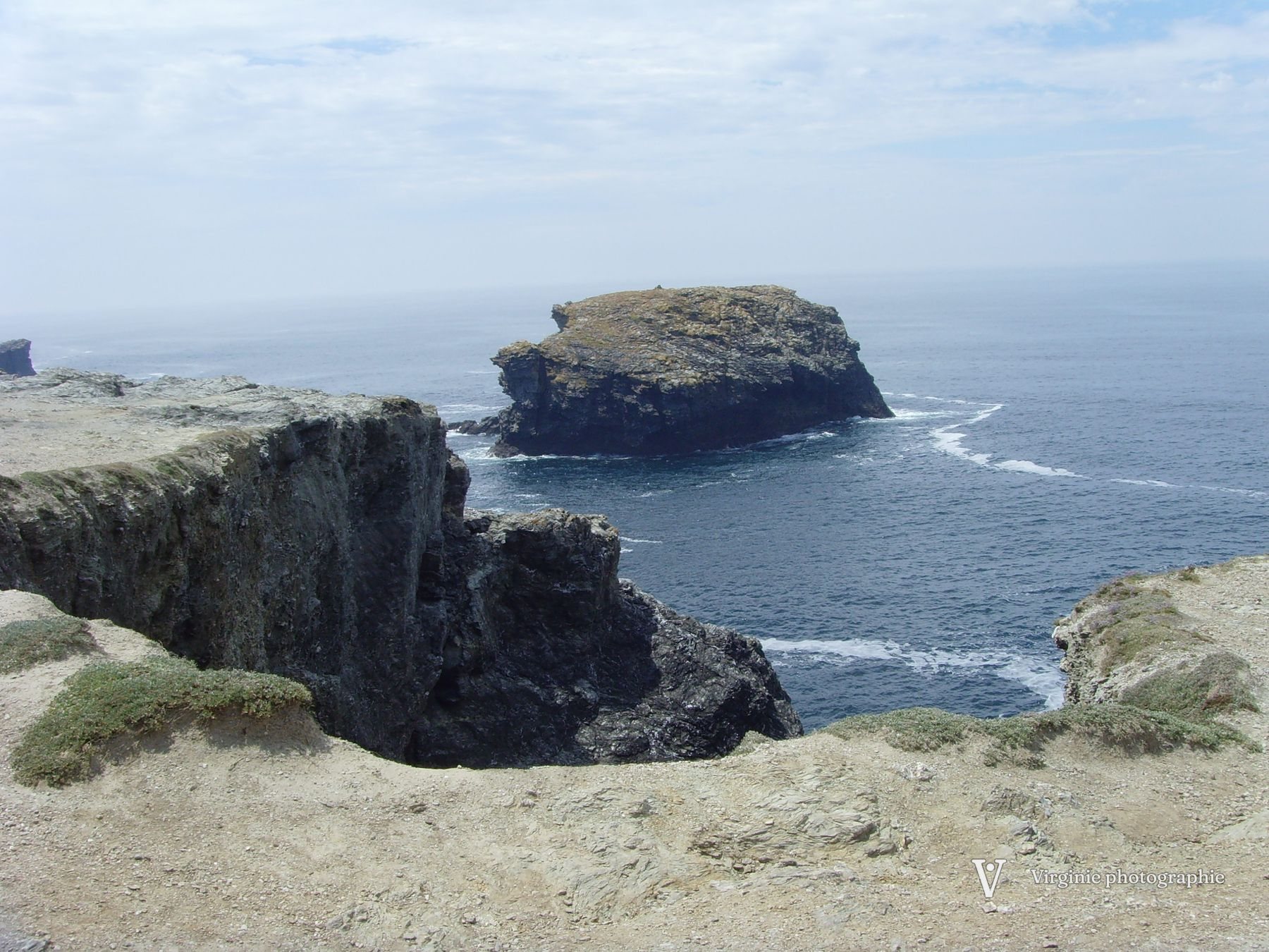 Un gros rocher posé dans l’océan, au pied d’une falaise