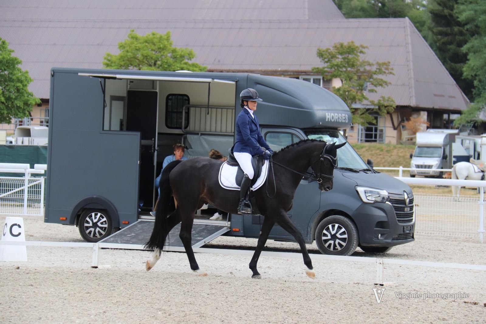Une cavalière et sa jument noire passent devant un van