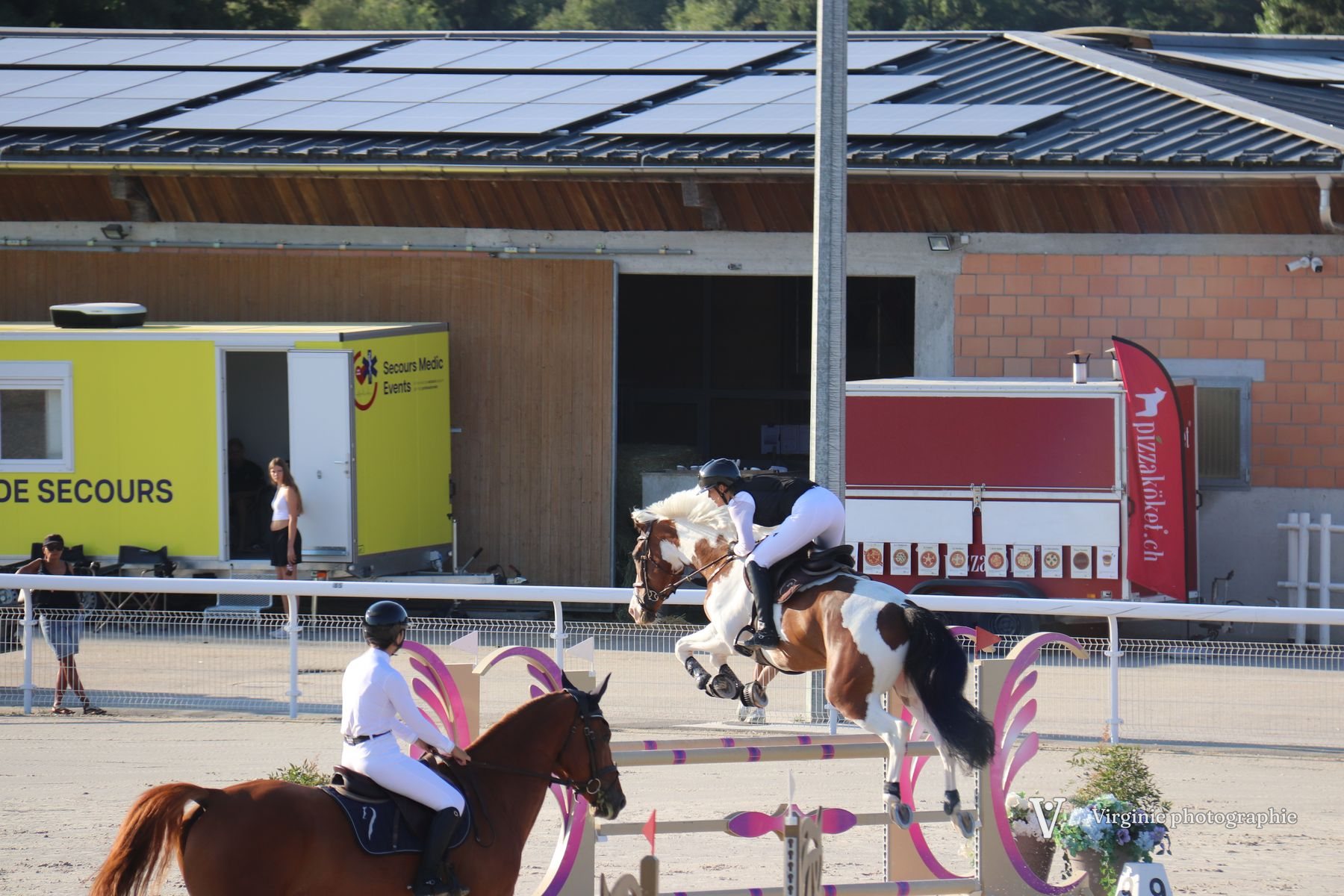 Un cheval pie franchit un obstacle de concours, un autre attend devant