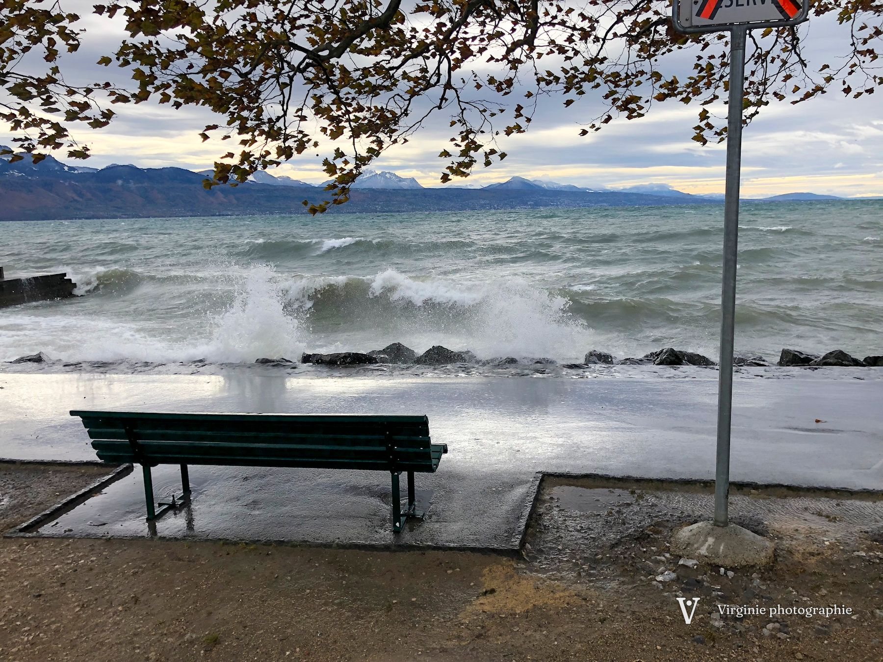 De grosses vagues se brisent sur le quai, un banc vide au premier plan