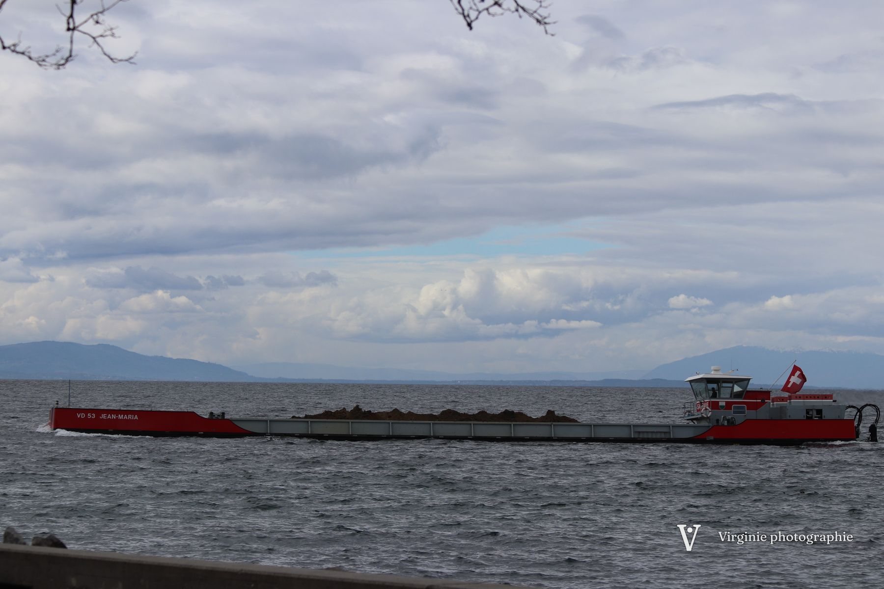 Des rayons de lumière percent les nuages sombres au-dessus du lac, un bateau rouge au loin