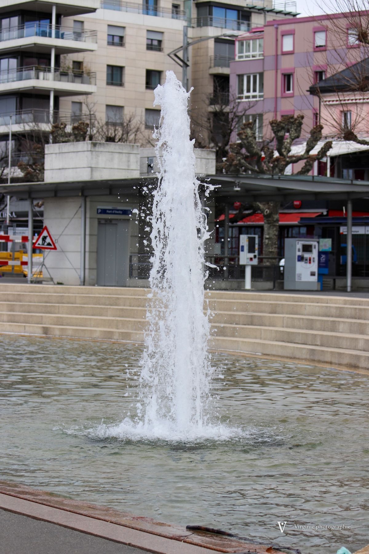 Un jet d’eau jaillit d’un bassin, devant des immeubles